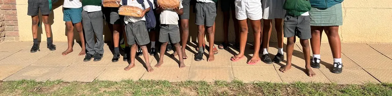Children in school uniforms, many barefoot, holding loaves of bread